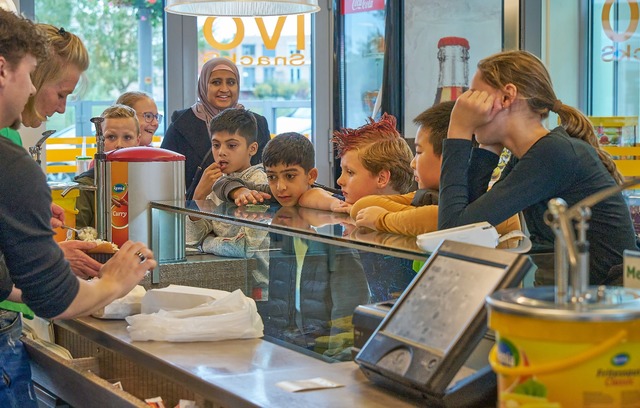 Een groep kinderen kijkt mee over de toonbank naar twee medewerkers in een snackbar bij de Talenten Academie